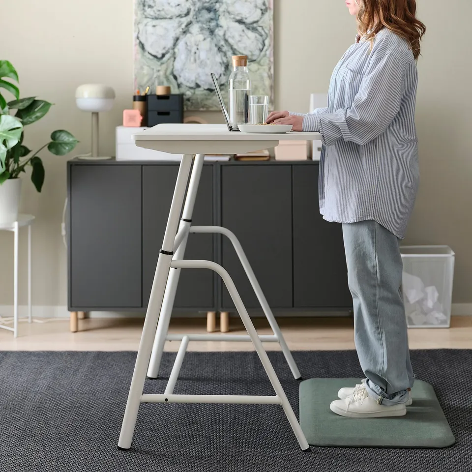 Person using height-adjustable standing desk with laptop, promoting ergonomic work.