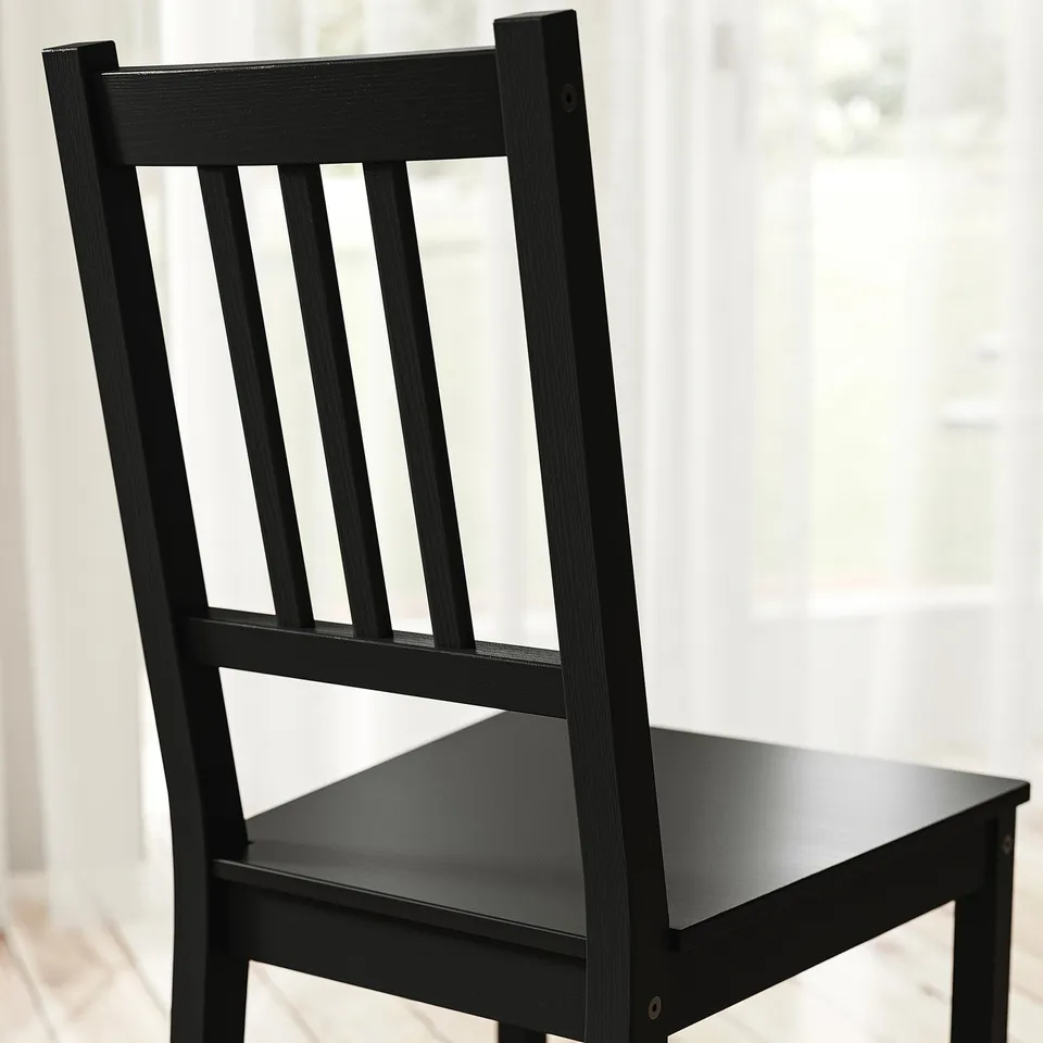 Black wooden chair with vertical slatted back and seat, posing near a window, showcasing its sturdy design and natural finish.