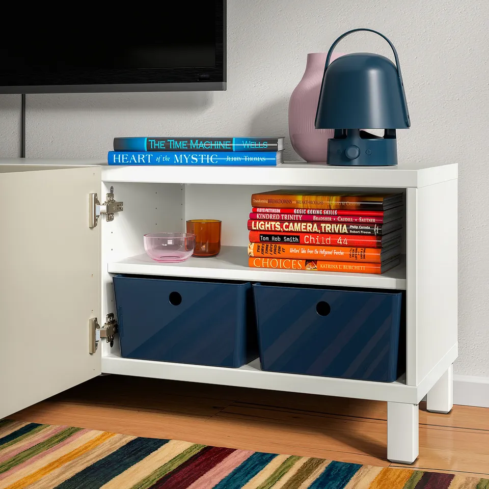 Small white shelf storing books, decorative bowls, and a blue lamp, showcasing KUGGIS organisational boxes.