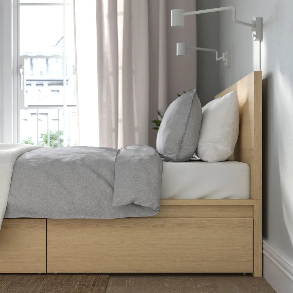 Image a modern bed with headboard, white pillows, grey blanket, and wall-mounted lights.