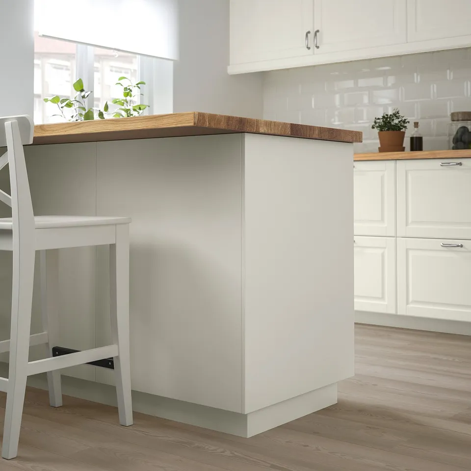 Modern kitchen scene with FÖRBÄTTRA white island, light wood countertop, simple stool, and minimalist decor; island smaller than cabinets.