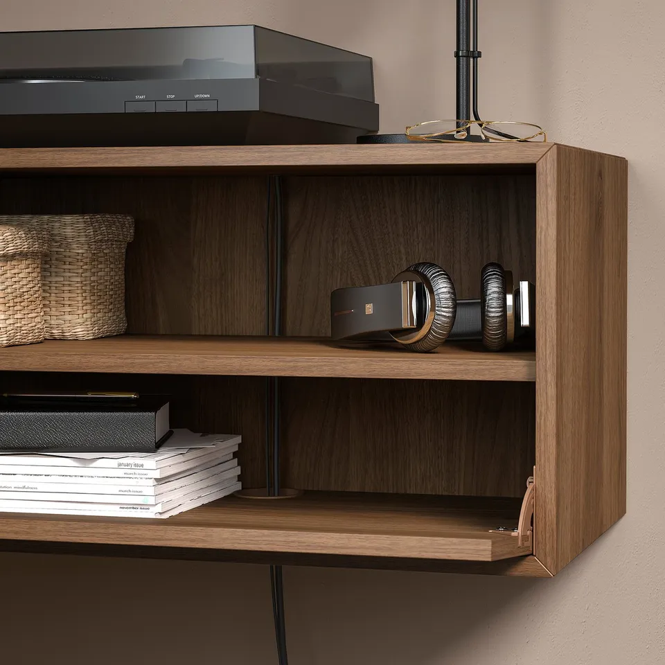 Wooden wall unit with open shelves displaying books, headphones, boxes, and a lamp.