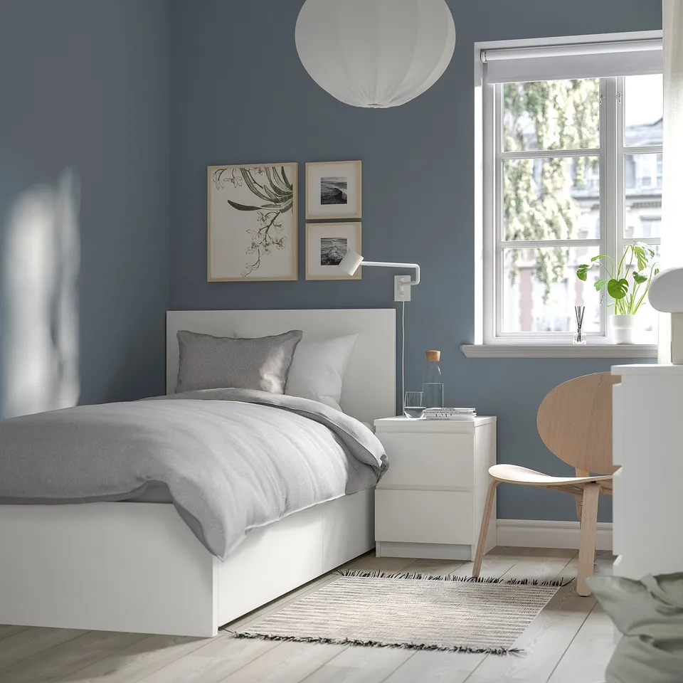 Modern minimalist bedroom with MALM white bed, grey bedding, blue walls, wooden chair, and large window. Simple and clean design.