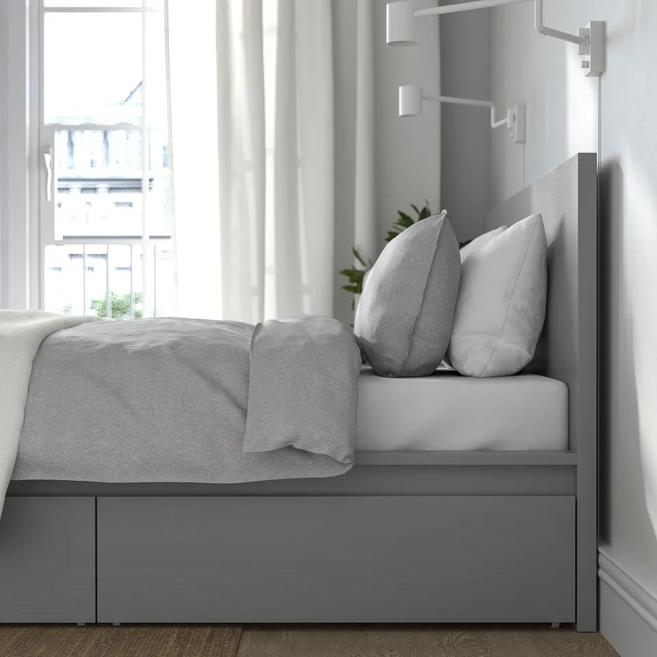 Minimalist bed with grey headboard and drawers for storage. The bed has built-in leds and pillows on it.