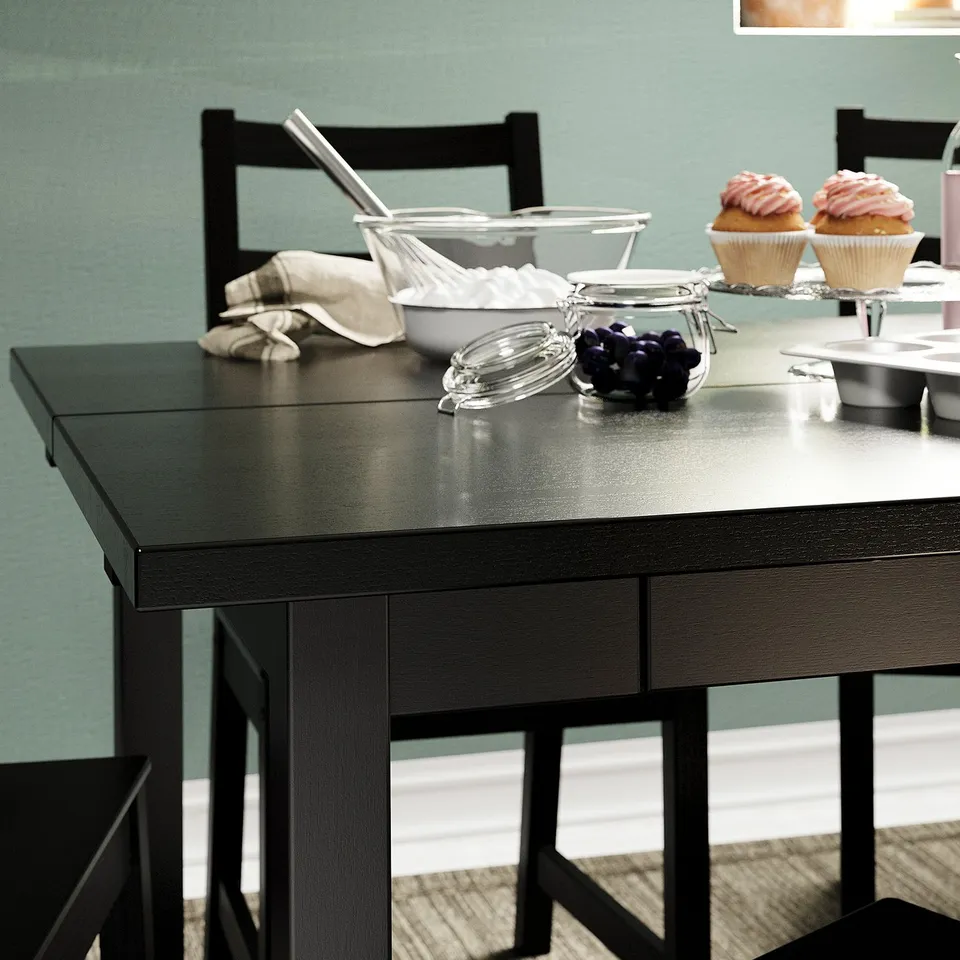 Modern black dining table with two chairs, a bowl of grapes, and cupcakes.