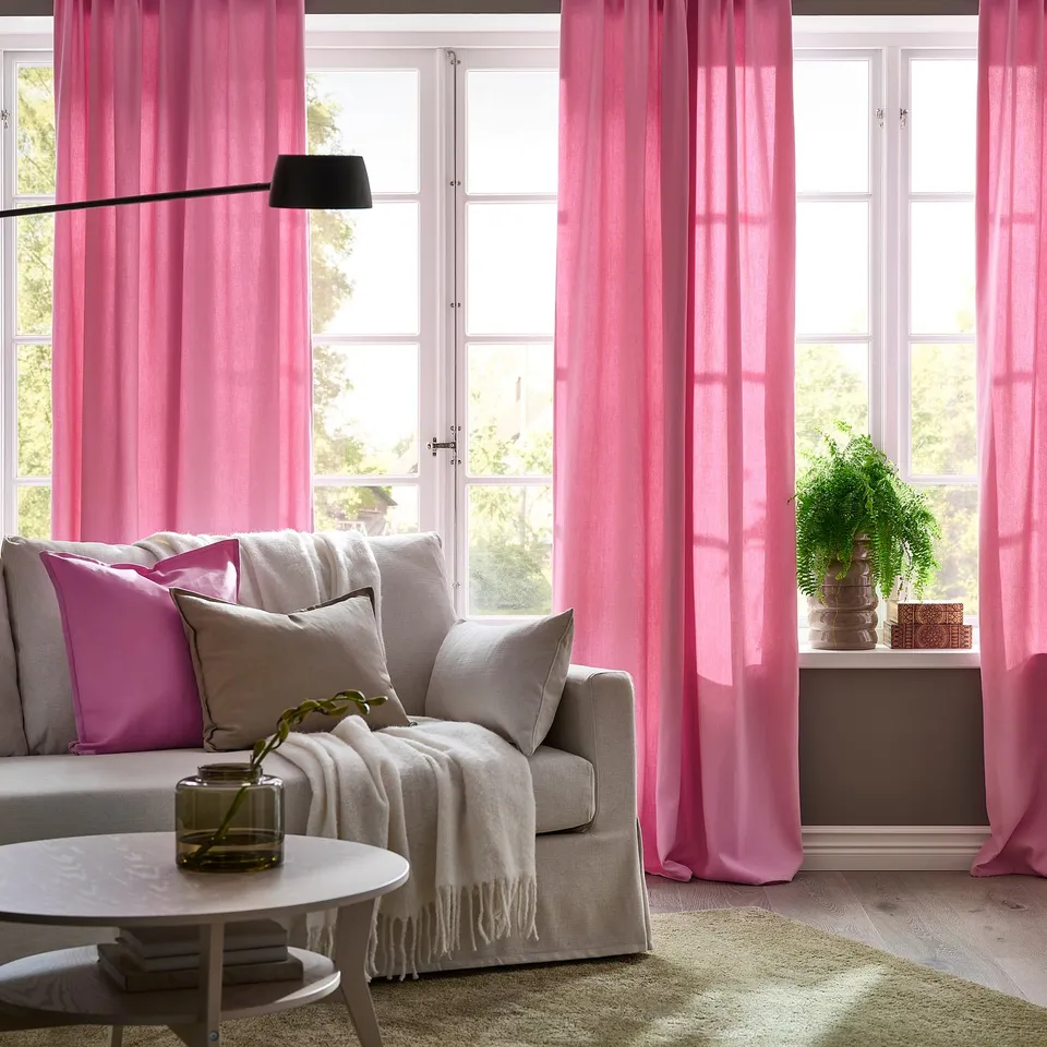 Pink curtains frame large windows, adding colour and privacy. Neutral armchair with pillows completes cosy, inviting space.