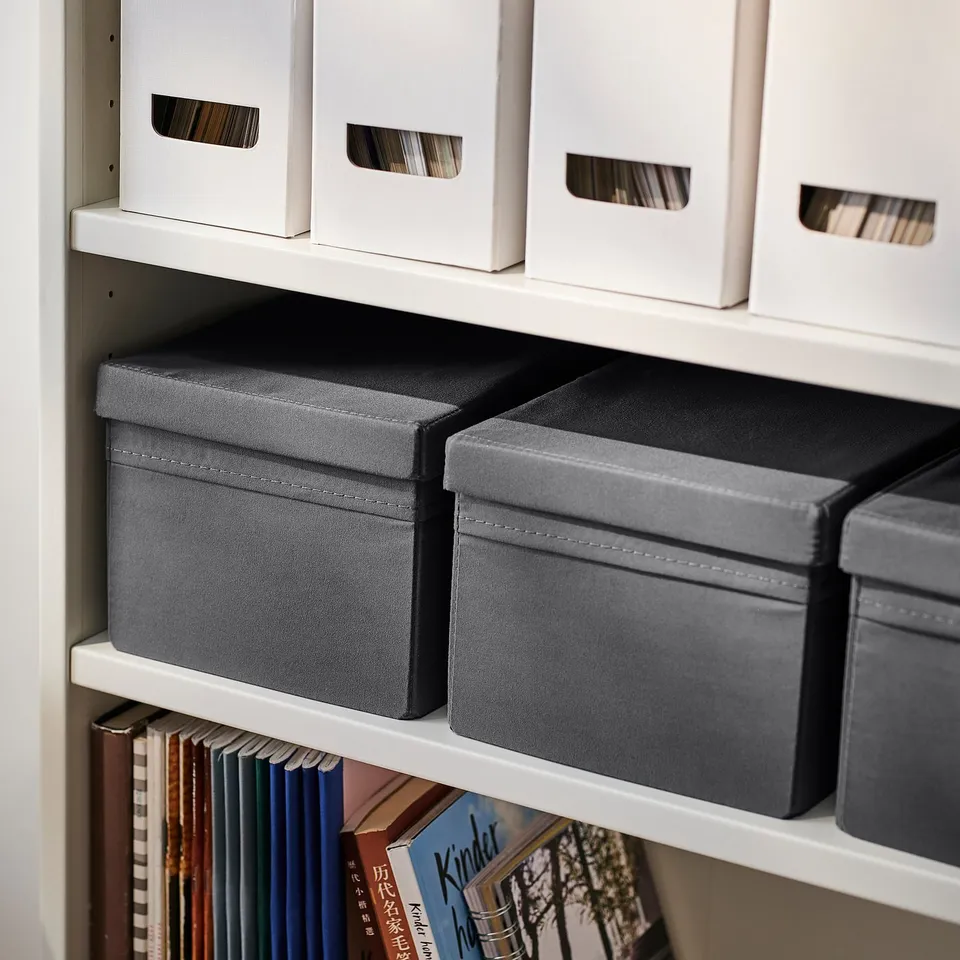 Shelf with grey fabric boxes and white containers, storing books and organising items.
