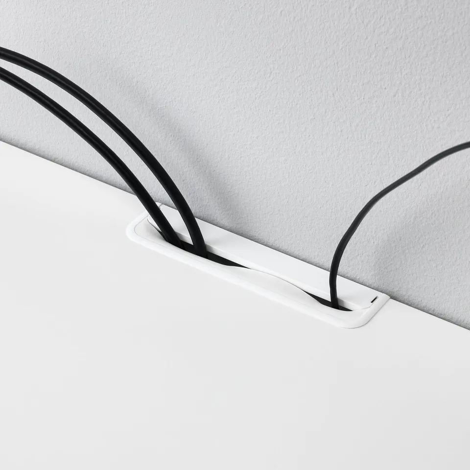 A close-up of a cord organiser on a white tv bench, holding black cables neatly in place.