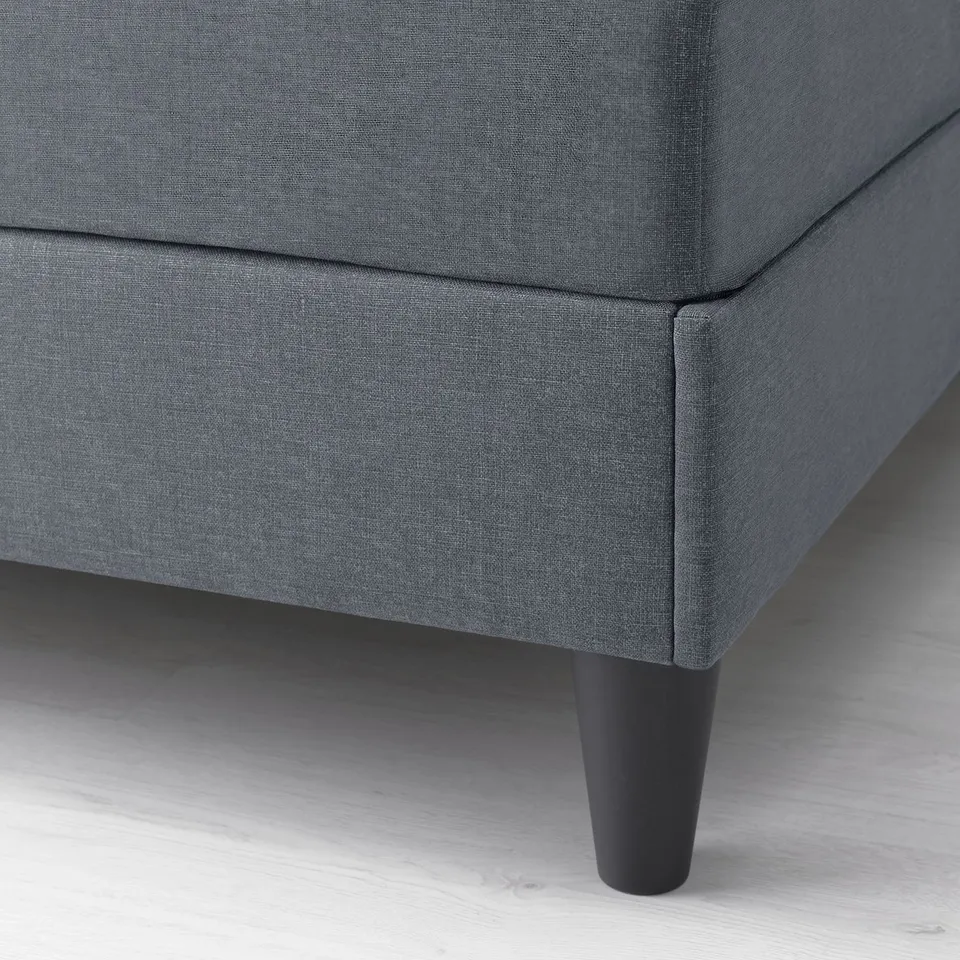 Close-up of grey upholstered bed leg, showing sturdy wood finish and padded support.