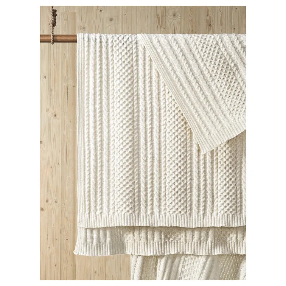 White SÖRBYSKOGEN recycled polyester knit throw draped over wooden wall rail.