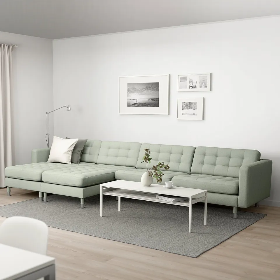 Green LANDSKRONA sectional sofa with cushions, wall photos, ottoman, coffee table with vase.