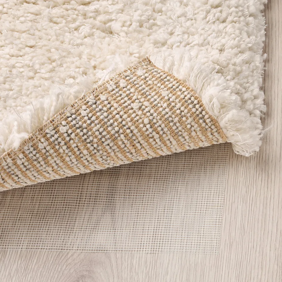 Close-up of thick, shaggy rug corner on wooden floor, showing piles and backing.