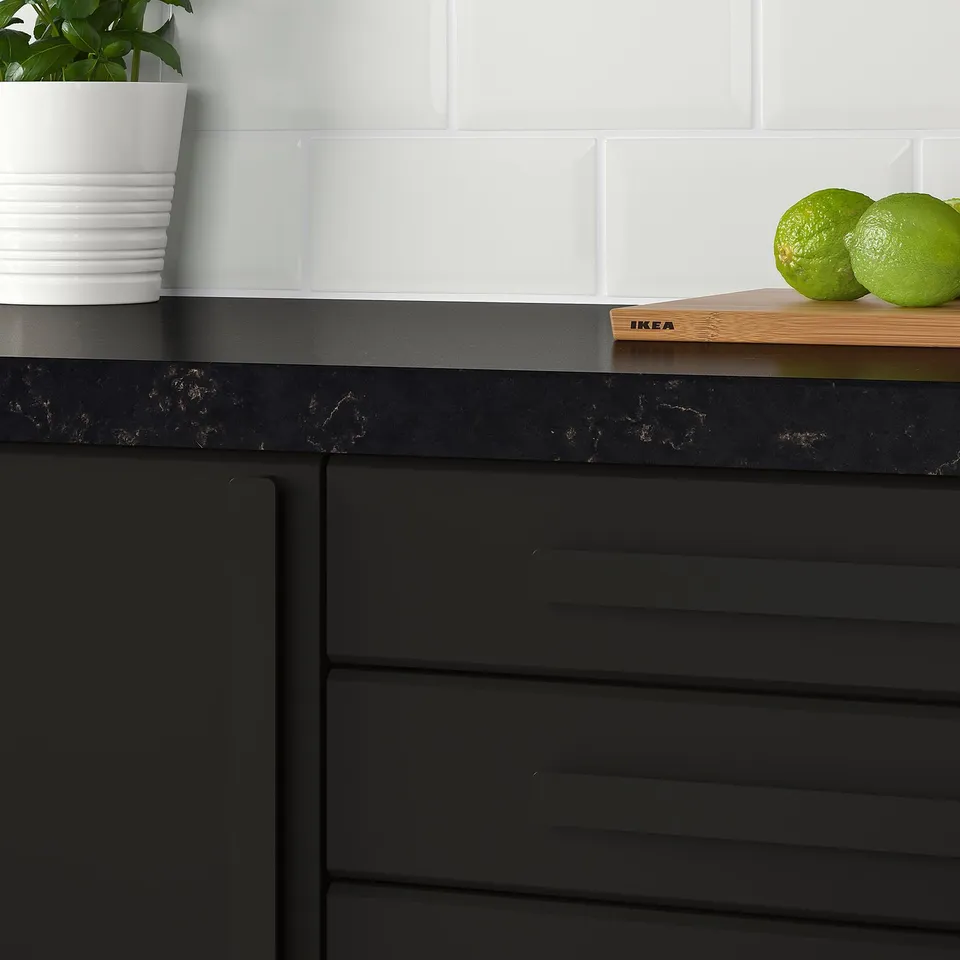 Modern kitchen counter with dark cabinets, white backsplash, lime fruits, plant, and handles.