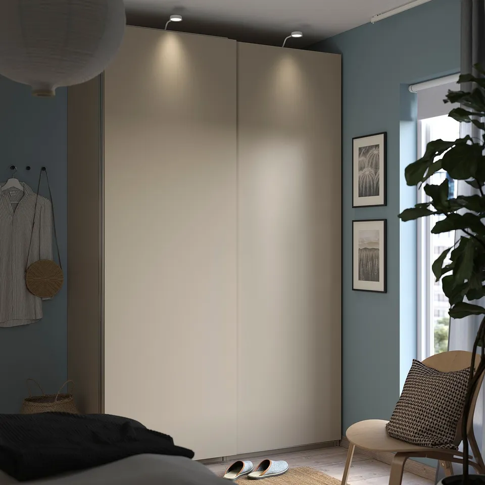 Minimalist bedroom with sliding wardrobe, striped shirt, round lantern, and framed art, cosy chair, plant.