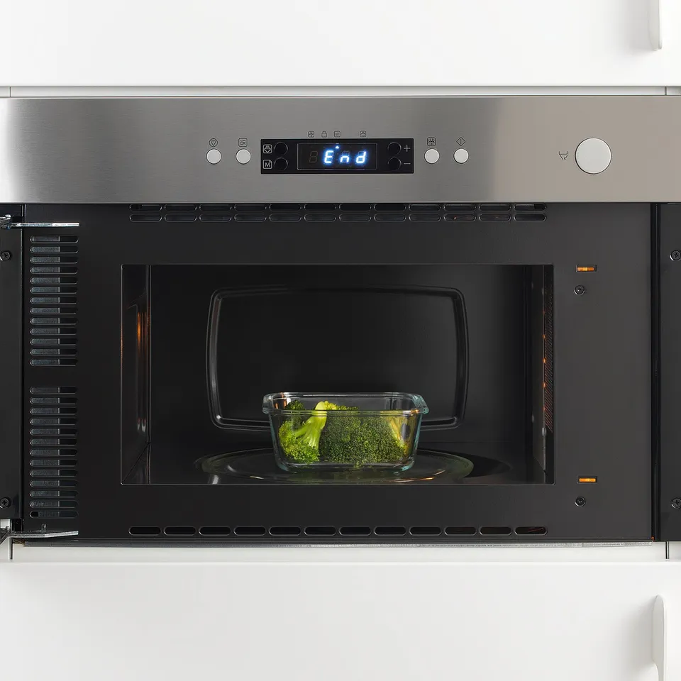 Built-in stainless steel microwave by IKEA 365+, displaying a digital clock and heating a glass container with broccoli.