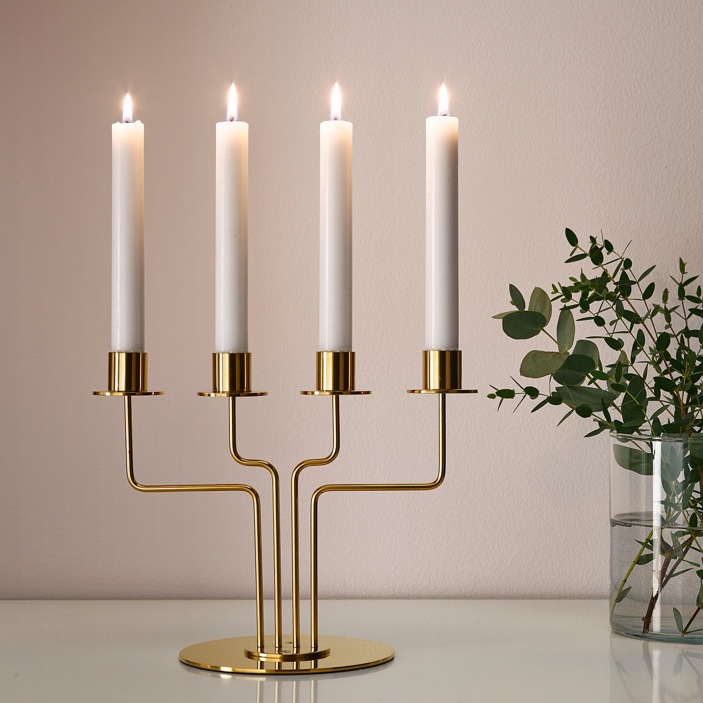 Gold candelabra with four lit white candles on a white table, adding warm atmosphere.