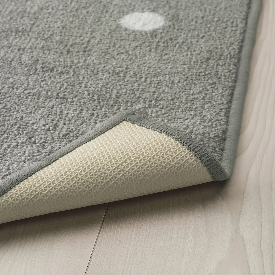 A grey rug with white dots, designed for children. The rubber backing prevents slipping, ensuring safety during play.