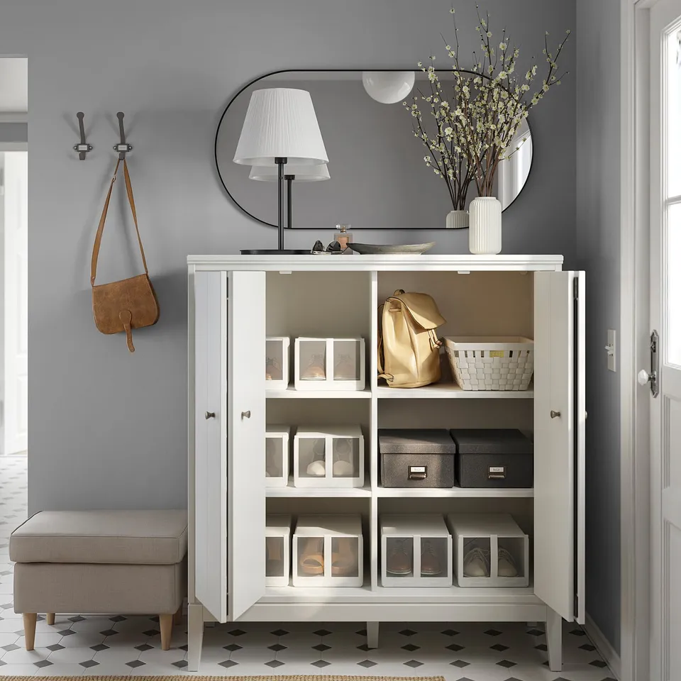 Modern entryway setup with white IDANÄS cabinet storing items, include lamp, mirror, floral decor, coat hooks, and bench.