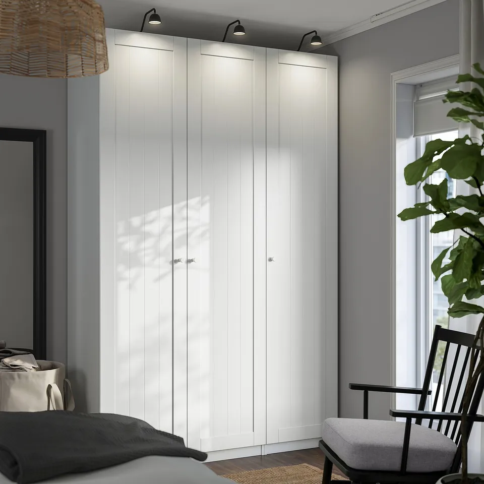 Minimalist bedroom with large PAX wardrobe, dark grey walls, pendant light, rocking chair and plant.