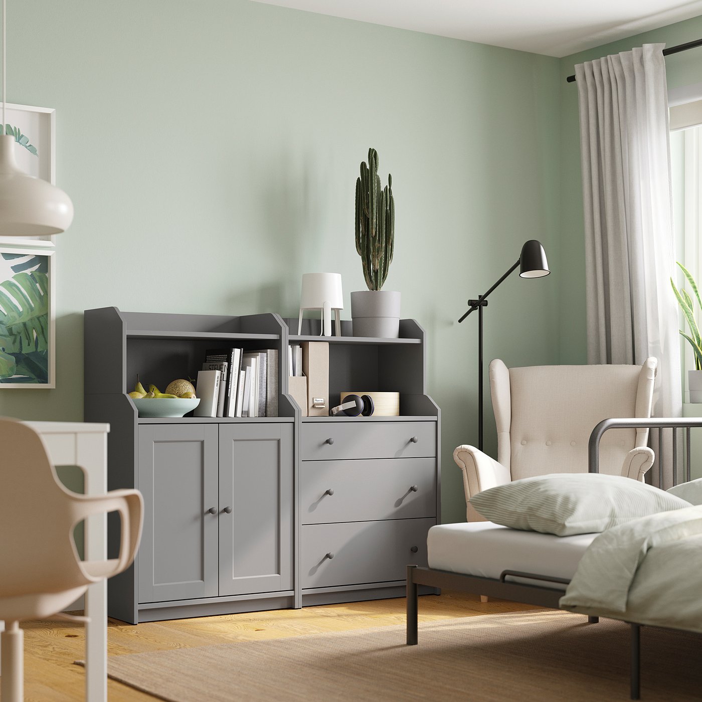 Modern living room with grey HAUGA storage, books, decor, white armchair, green walls, cactus.