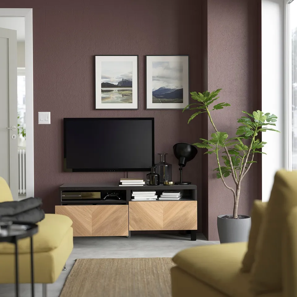 Modern living room with yellow armchairs, tv on wood console, nature prints, and a large plant.