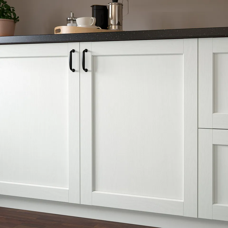 White kitchen cabinet with black handle, countertop items, and plant.