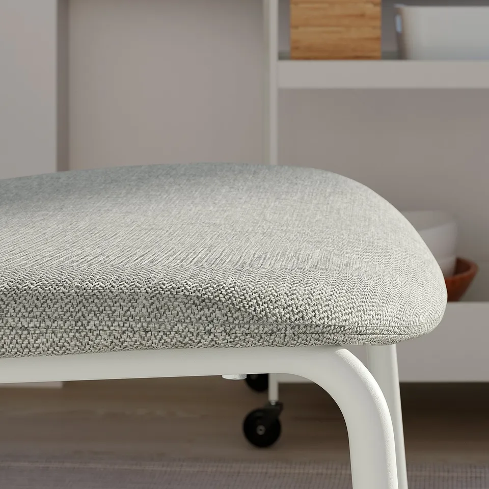 Close-up of a modern, cushioned stool with white metal legs on wheels.