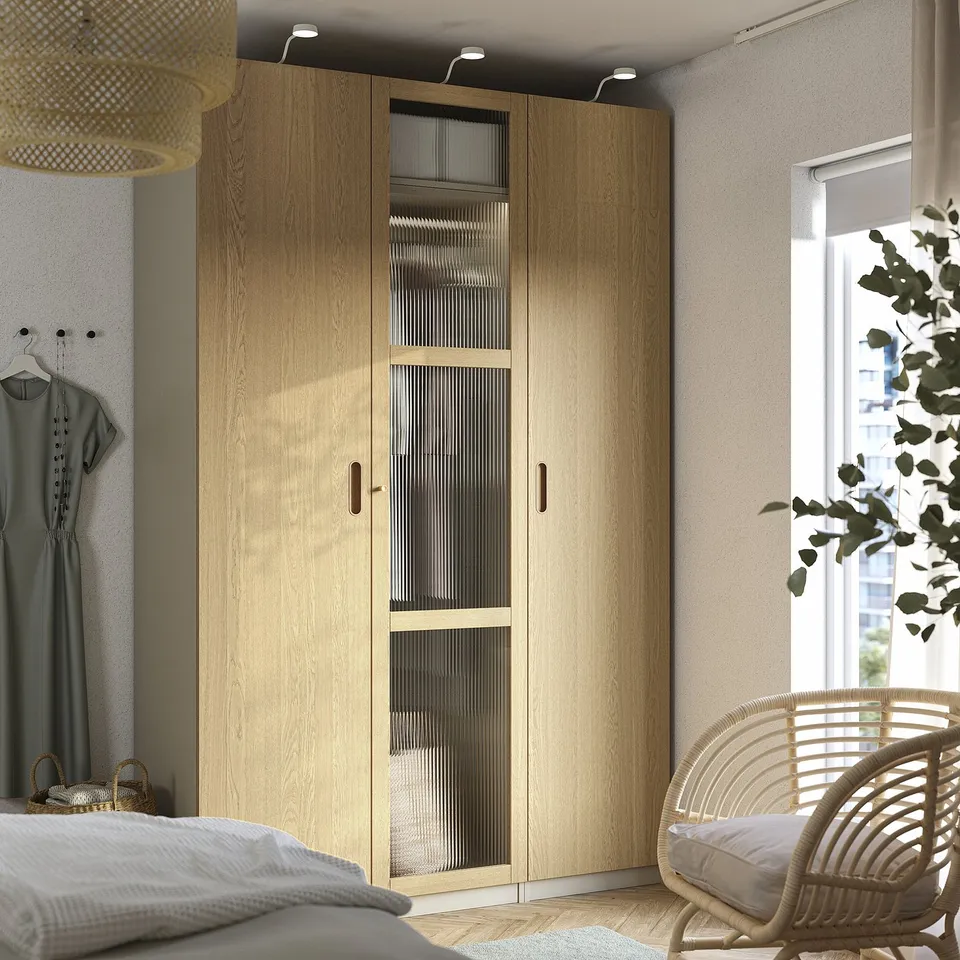 Modern PAX wardrobe with glass, lighting, & mesh baskets in bedroom.