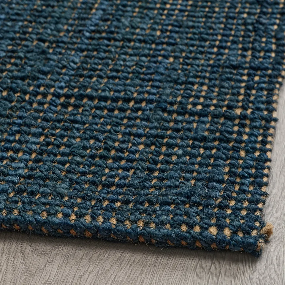 A close-up of a flat-woven, dark blue jute rug. Its intricate weave and natural texture are visible, highlighting its quality and craftsmanship.