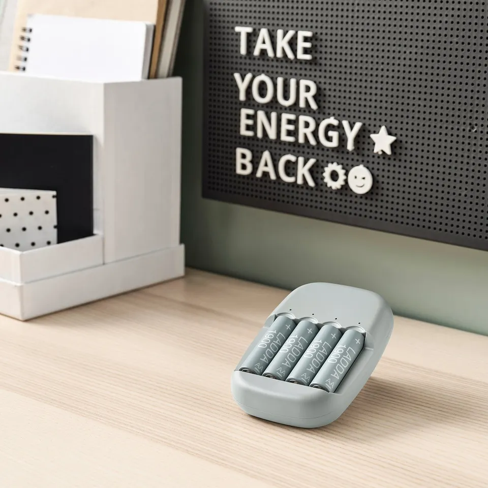 Grey STENKOL charger holds four batteries on desk, motivational letterboard behind.