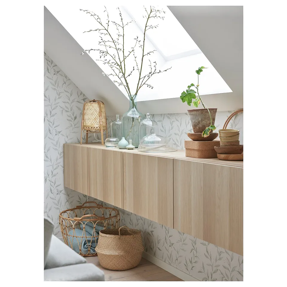 Modern living room with light wood tv unit, green plants, wicker baskets, and stylish decor against leaf-patterned wallpaper.