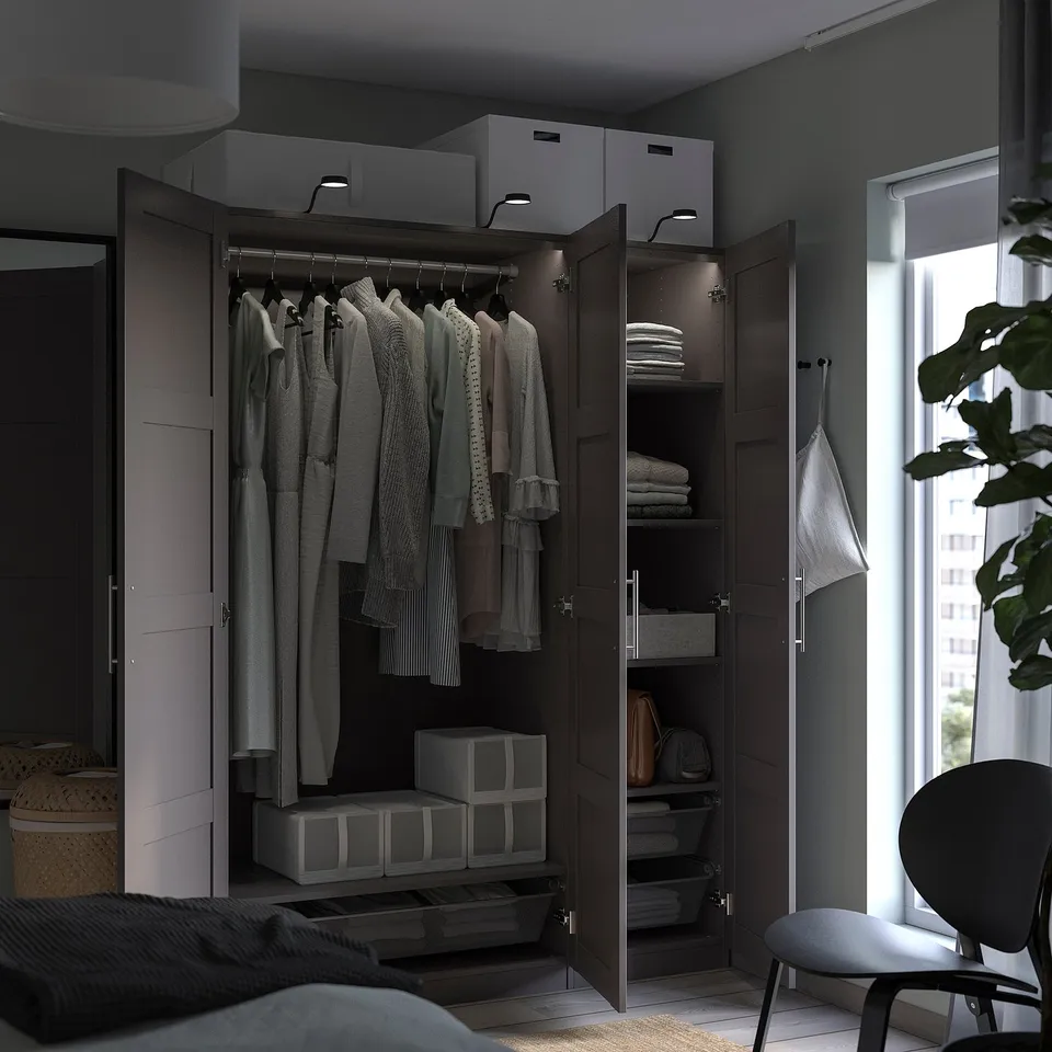 Modern bedroom with dark brown PAX wardrobe, clothes, and accessories inside, featuring shelves and drawers.