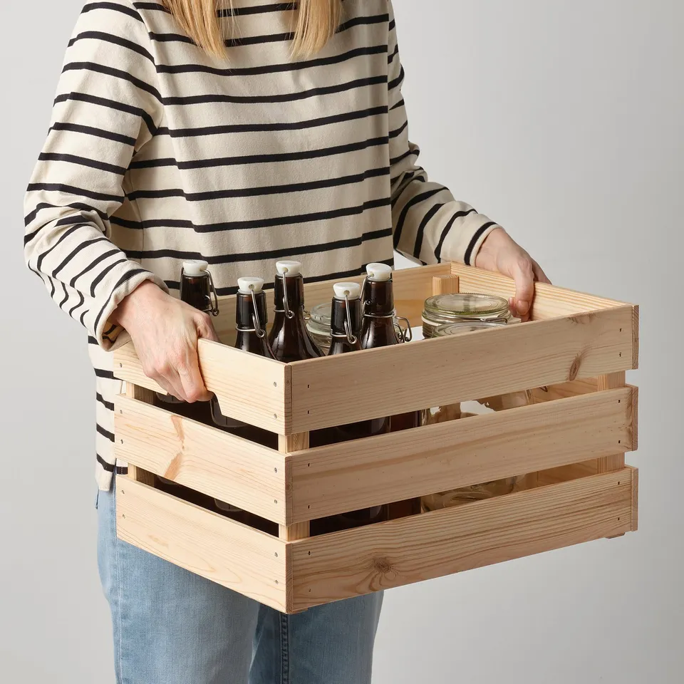 Person holding wooden crate with bottles, showing sturdy and durable storage.