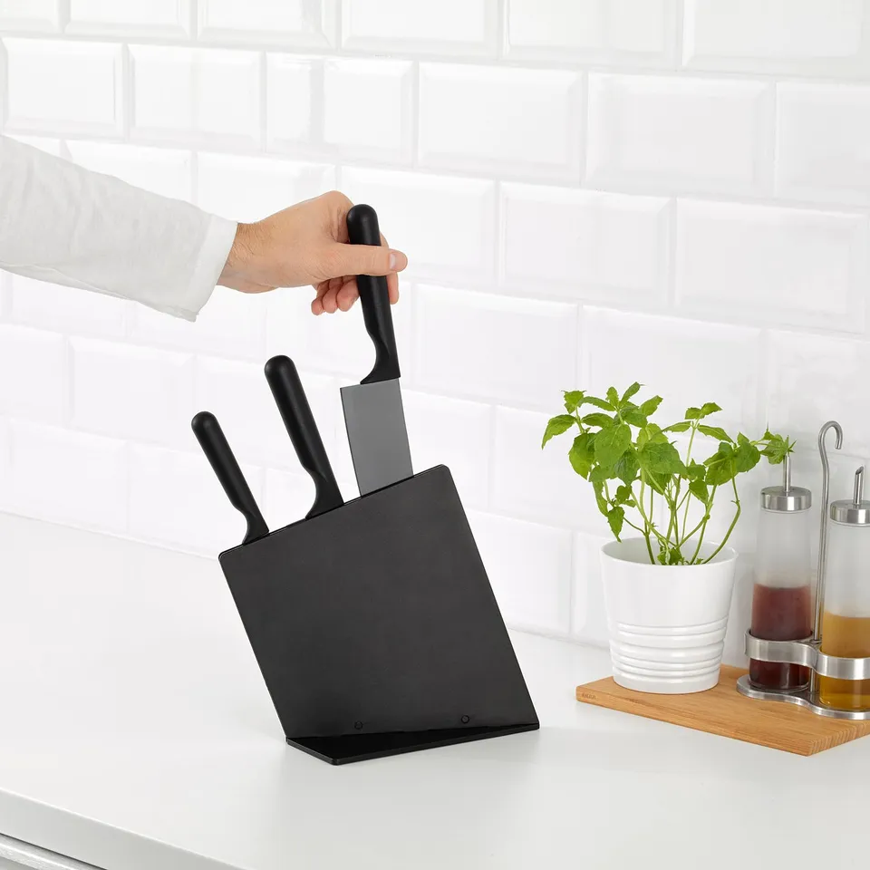 Person holding a chefs knife from a magnetic black knife block on a kitchen counter, next to a plant and oil dispensers.