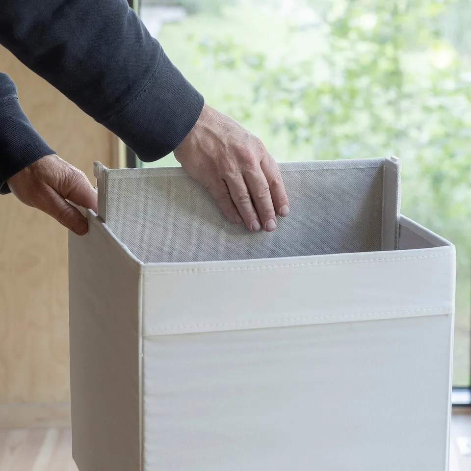 Hands placing a removable divider inside a storage box, dividing it into sections.