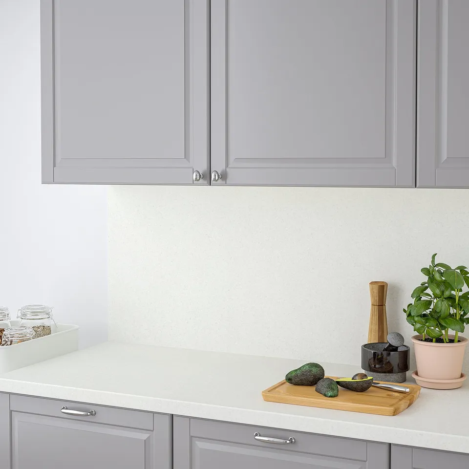 A modern kitchen counter with a light grey, speckled worktop. It has rounded edges, and displays avocados, a cutting board, a plant, and spice jars.