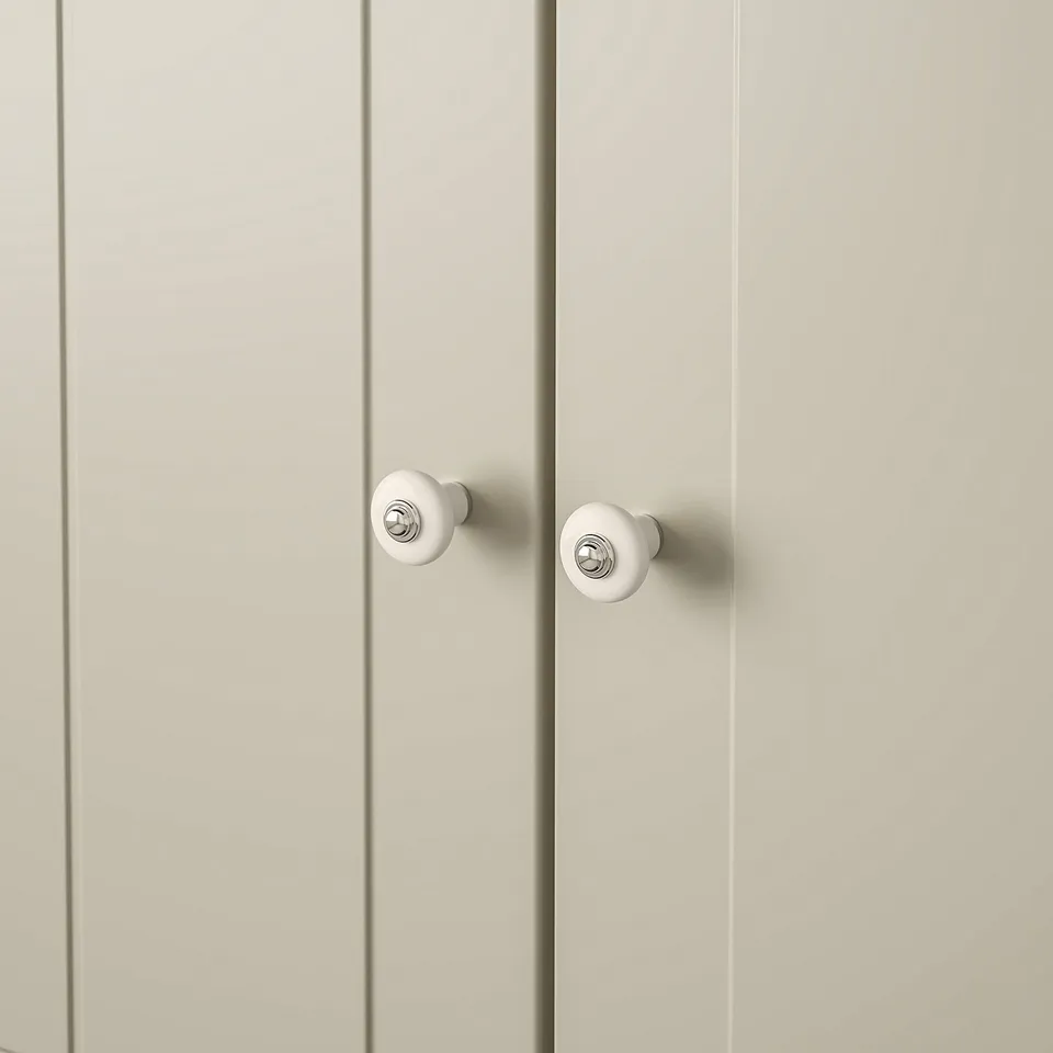Two elegant white knobs with chrome accents, mounted on a smooth, cream-colored cabinet door, showcasing a high-quality, classic design.