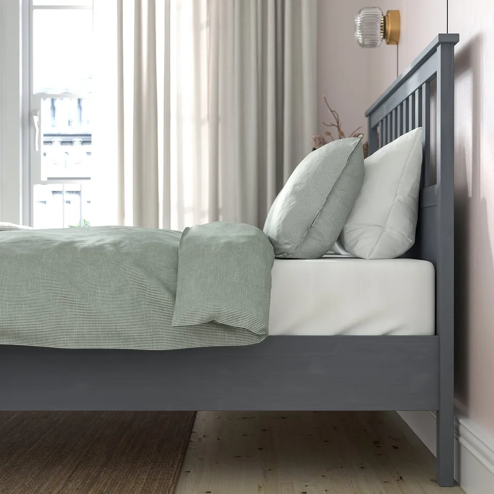 Bedroom with grey HEMNES wooden bed, white pillows, light grey curtains, and city view from window.