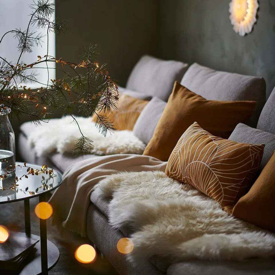 Cosy sofa with plush cushions, warm lights, and pine branches. Perfect for holiday relaxation.