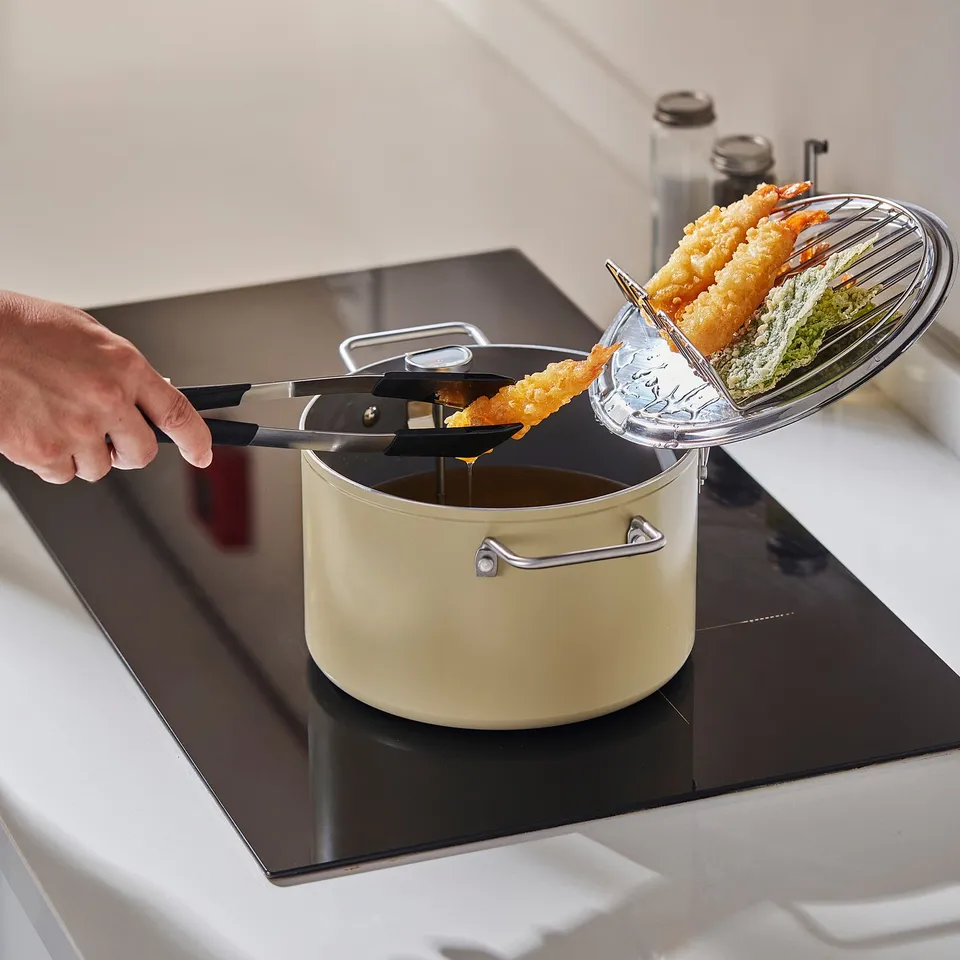 Person is frying food in SKÄGGTORSK pot on stove. Pots oil philtre rack drains oil from food.