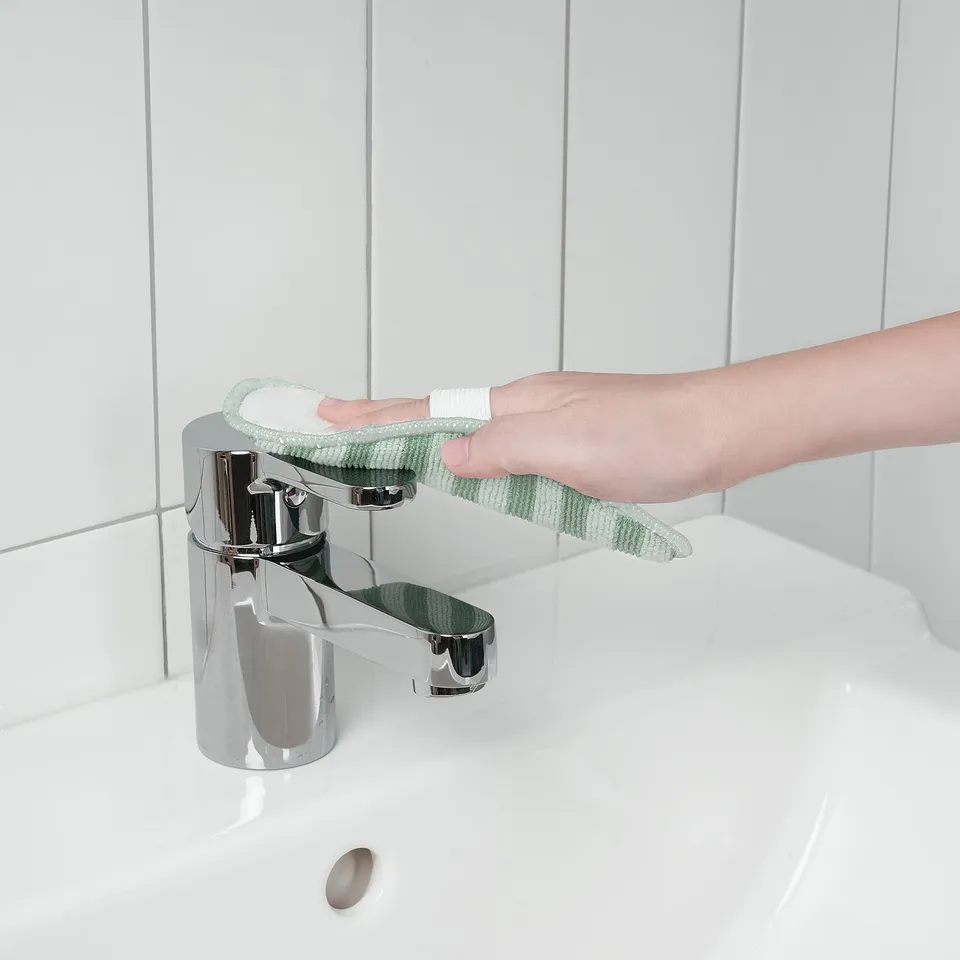 A hand cleans a tap with a green PEPPRIG microfiber pad, ensuring a scratch-free shine.