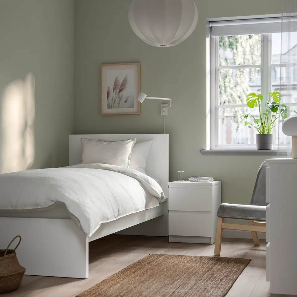 Minimalist bedroom with green walls, white MALM bed, beside table, and chair. Large window with plant.