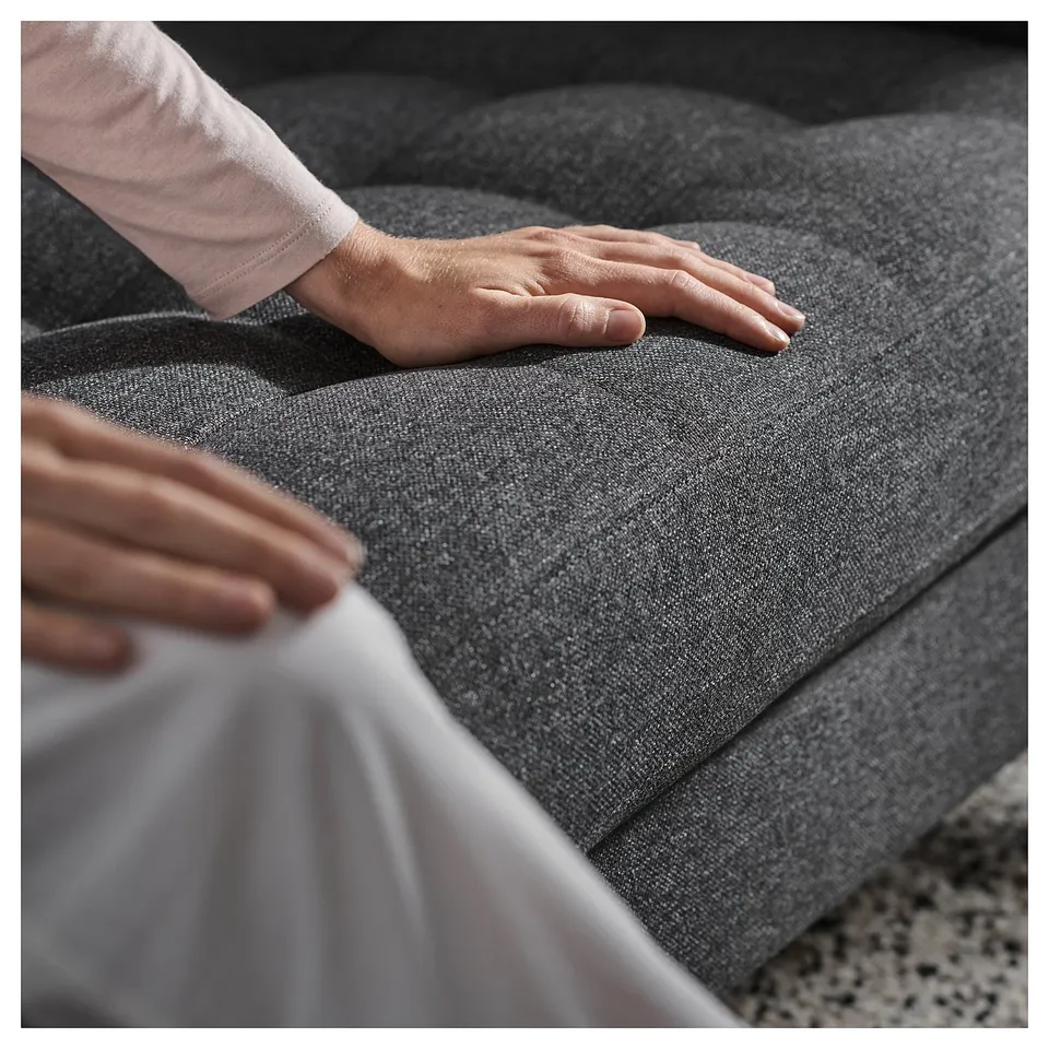 A person adjusting a dark grey fabric sofa with light-colored hands visible.