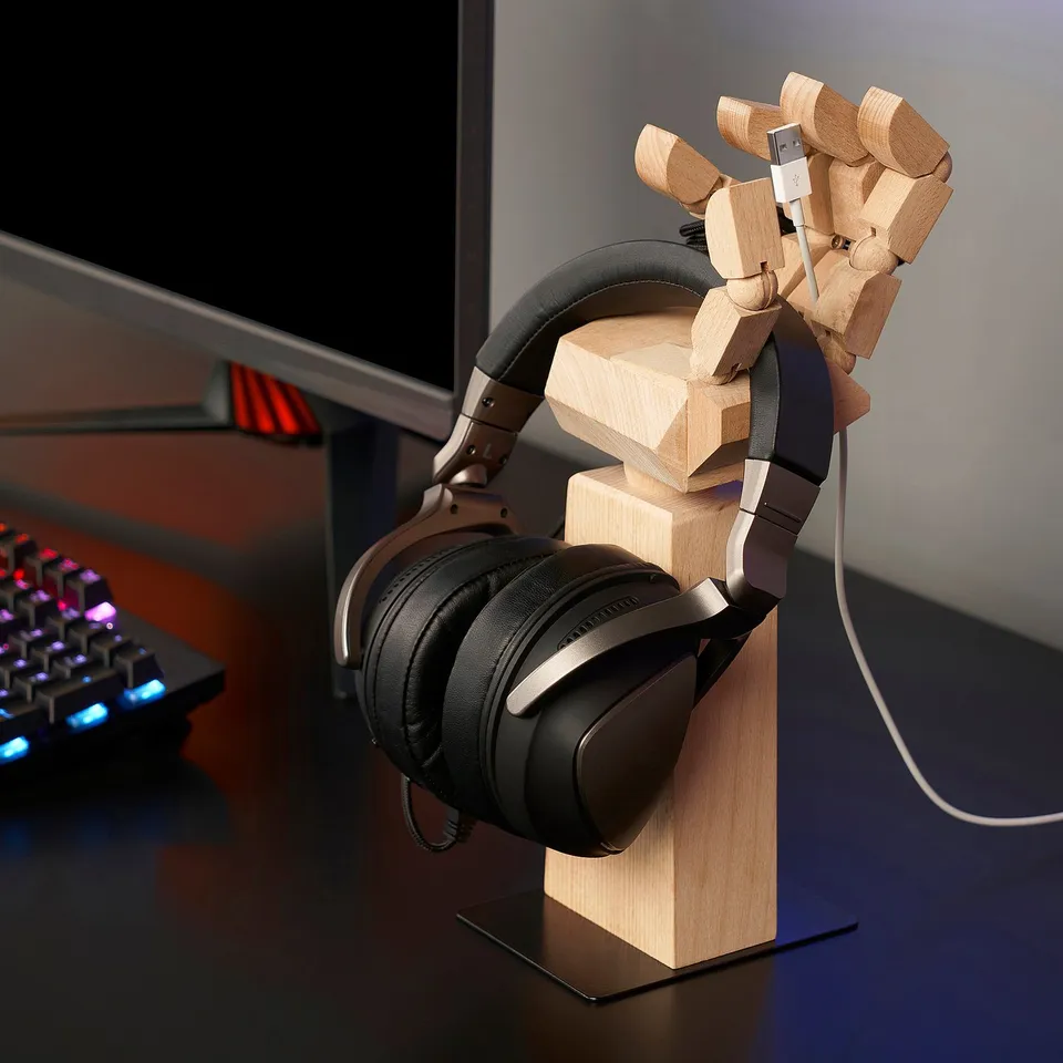 Wooden desk organiser shaped like a hand holding a headset and a usb drive, keeping items off the desk.