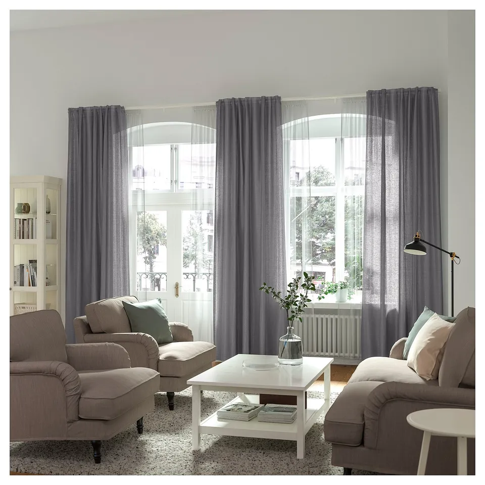 Modern living room with grey VIDGA curtains, tan couches, and a floor lamp. Natural light creates a bright, cosy ambiance.