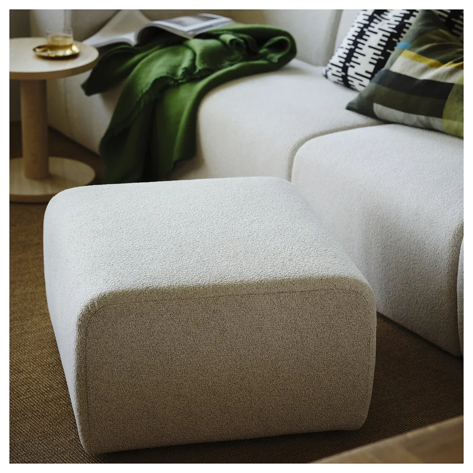A modern white stockh19lm 2025 sofa with a green blanket and pillows. Its a medium-sized piece, smaller than the side table.