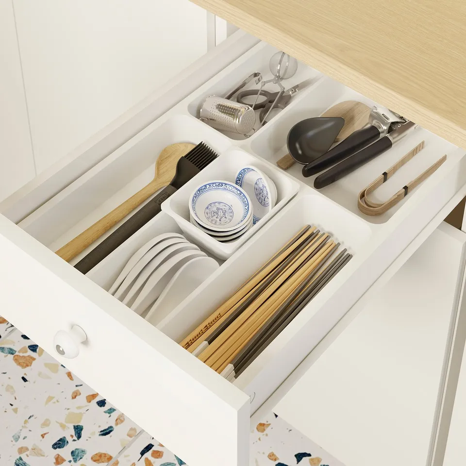 White kitchen drawer with organised utensils and plates, part of IKEA KNOXHULT modular setup.