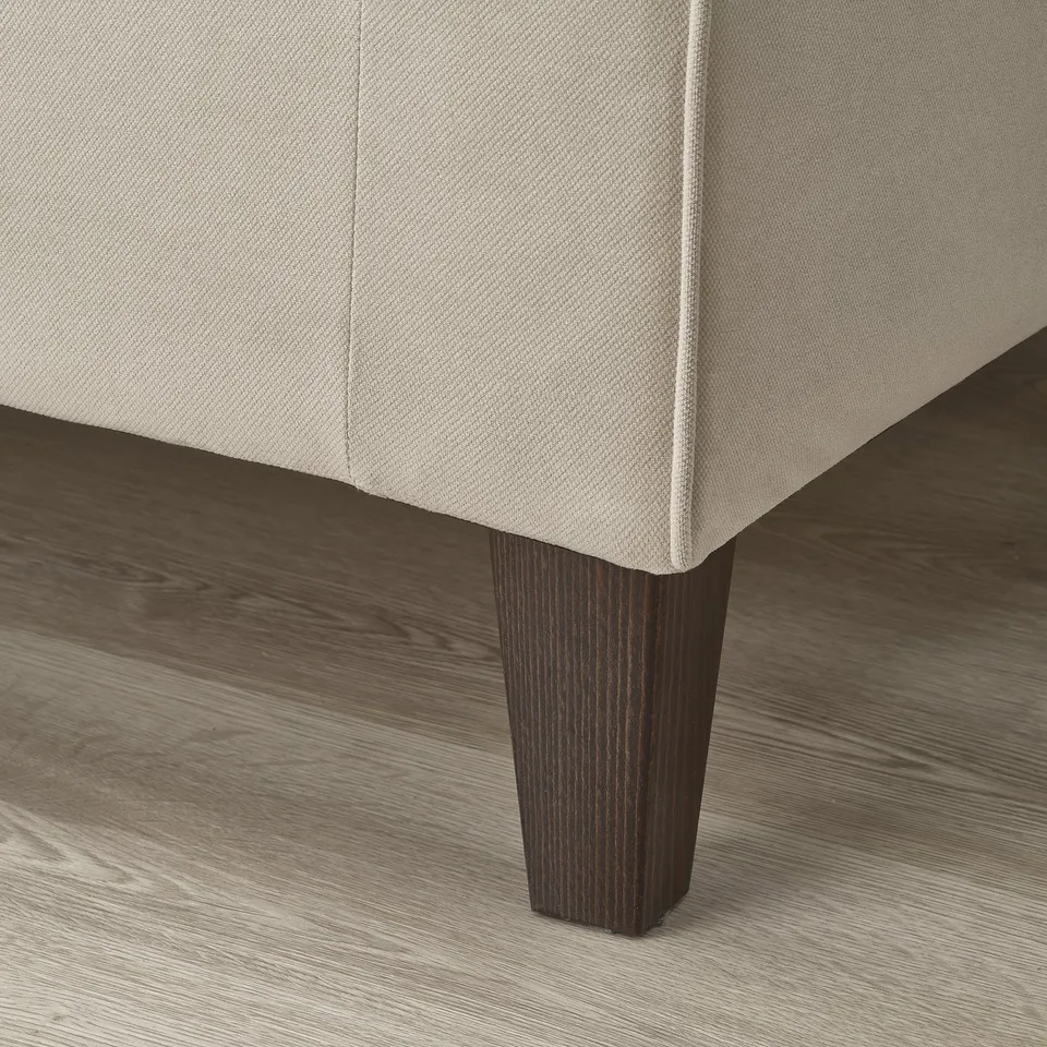 Sofa detail: sleek, beige upholstery with sturdy, dark wooden legs; smooth fabric, elegant design.