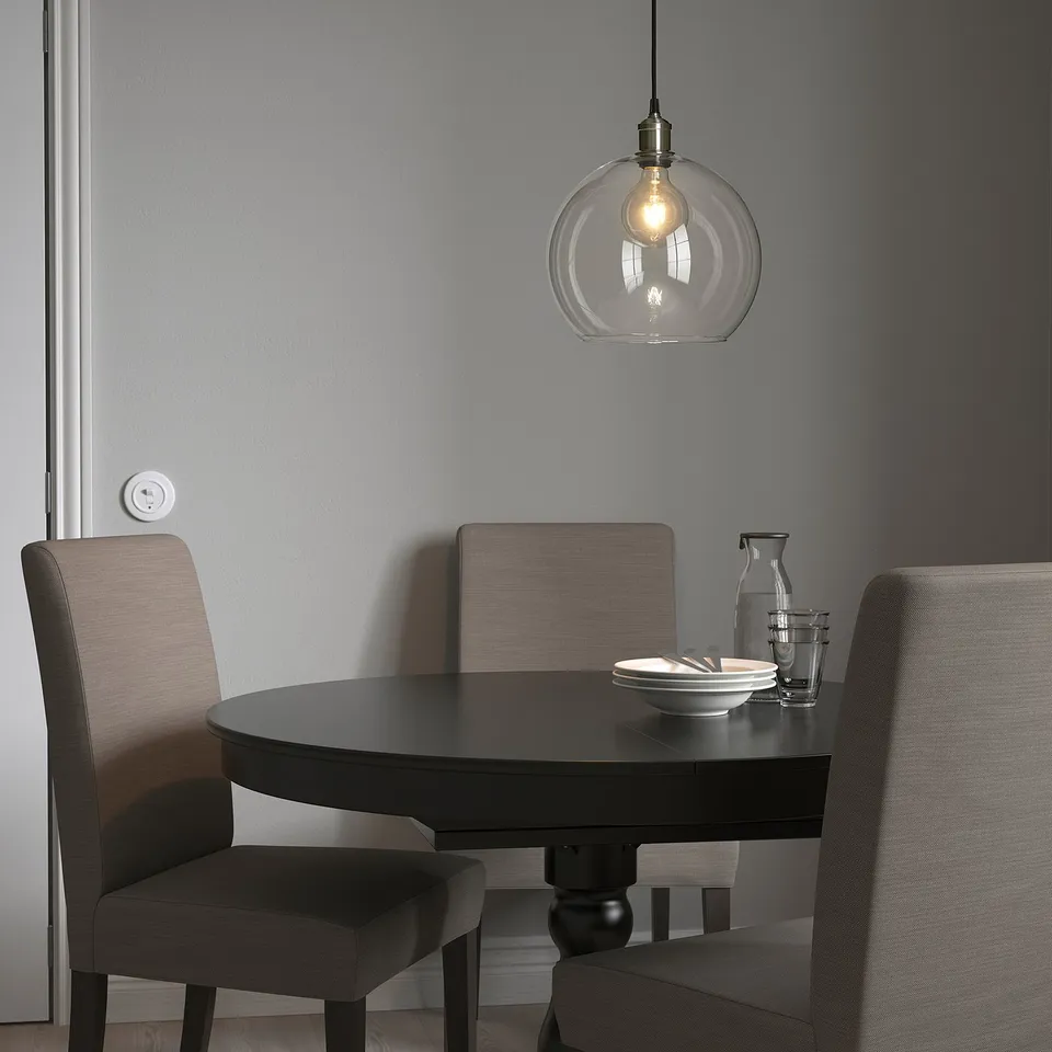 Modern dining area with black round table and grey chairs, featuring a JAKOBSBYN glass pendant lamp and warm lighting.