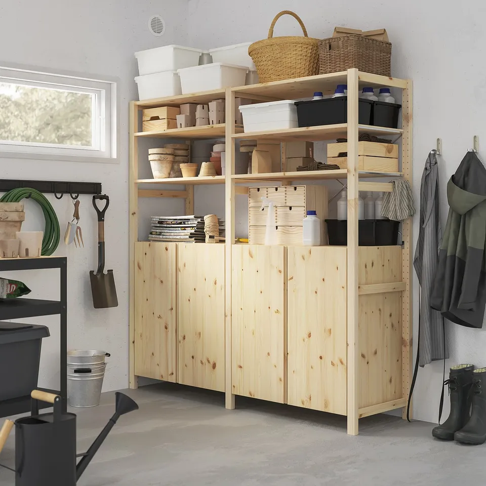 Wooden IVAR storage furniture. Shelves hold plastic bins and baskets. Large, natural pine finish. Clothes and tools hang beside it.